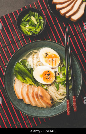 Ramen zuppa di noodle al pollo e uovo servite nella ciotola sul tappetino di bambù. Tabella Vista dall'alto. Cucina asiatica Food Foto Stock