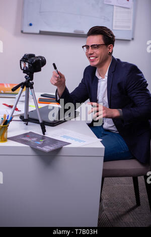 Ridendo imprenditore positivo portando pennarello nero e dispositivo di puntamento con esso Foto Stock