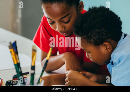 Primo piano di elementare African American kids creativamente il disegno e la Pittura con pennelli e pastelli - bambini creativi concetto di istruzione Foto Stock