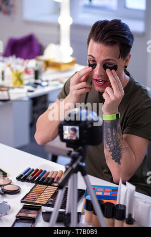 Curioso straordinario uomo seduto al tavolo circondato con il trucco Foto Stock