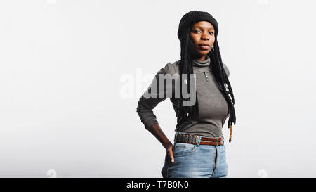 Ritratto di una donna africana in jeans e maglietta con lunghi dreadlocks con gusci cowrie. Donna africana con la mano in tasca posteriore isolato su bianco Foto Stock