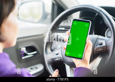 Femmina giovane conducente utilizzando il touch screen smartphone in un'auto. verde chroma key sul display del telefono cellulare. Foto Stock