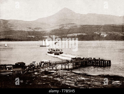 Un palazzo di fine ottocento vista di un battello a vapore del traghetto, legato per Ardrossan sulla terraferma scozzese lasciando Brodick Pier, sul Arran, con capra cadde, il monte più alto dell'isola. L'isola di Arran è la più grande isola nel Firth of Clyde e la settima più grande isola scozzese. Storicamente parte della Buteshire, è ora in Ayrshire Foto Stock