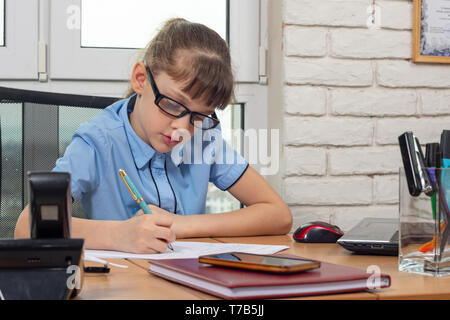 Un otto-anno-vecchia ragazza al tavolo in ufficio scrive una penna stilografica su un pezzo di carta Foto Stock