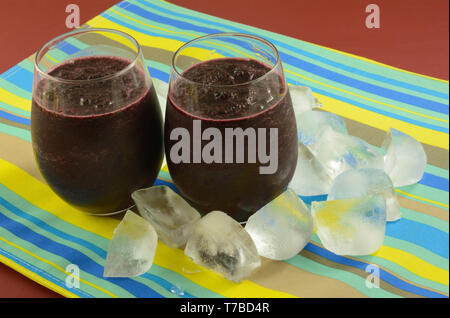 Due freddo frullato mirtillo ice bevande in bicchieri sul posto a strisce mat con cubetti di ghiaccio Foto Stock