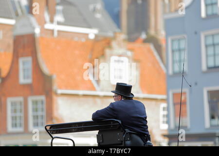 DELFT, Paesi Bassi - 22 Aprile 2019: Close-up su il cocchiere di una carrozza a cavallo, tradizionalmente condita e con facciate colorate in background Foto Stock