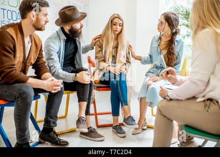 Giovane donna che piange durante la terapia psicologica con un gruppo di persone il suo supporto in ufficio Foto Stock