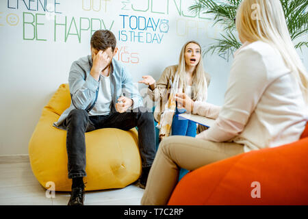 Coppia giovane avente incomprensioni durante la consultazione psicologica con psicologo femmina nell'ufficio moderno Foto Stock