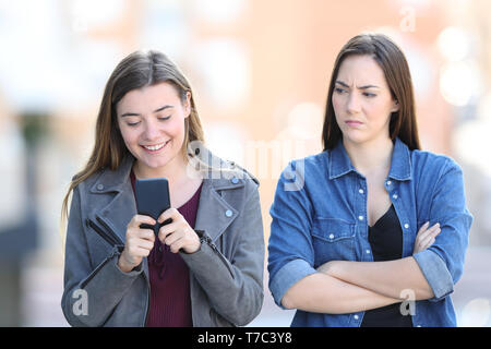 Vista frontale ritratto di una donna arrabbiato con il suo amico che sta utilizzando il telefono in strada Foto Stock