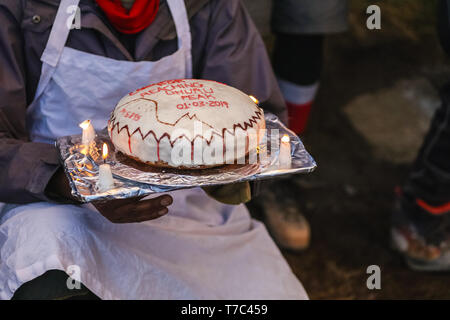 Chiudi immagine di una gustosa grande torta di compleanno con crema bianca e rossa con titolo auguri. Alcune candele accese sui lati. Amici riuniti per augurare Foto Stock