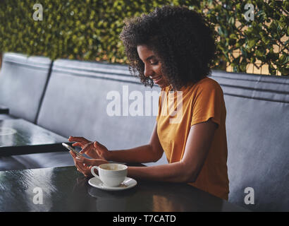 Una giovane donna africana utilizzando lo smartphone nel cafe Foto Stock