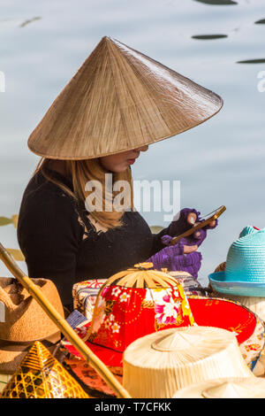 Damnoen Saduak, Tailandia - 4 Marzo 2017: Hat fornitore su telefono cellulare. Il mercato galleggiante è una meta turistica molto atrraction Foto Stock