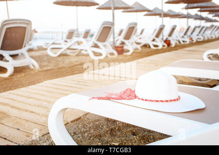 Vista su molte sedie a sdraio con estate cappello bianco su uno di essi. Foto Stock