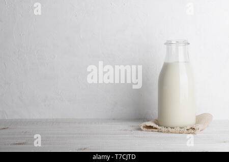 Bottiglia di latte su una tela di sacco su legno bianco sfondo tabella orizzontale con spazio di copia Foto Stock