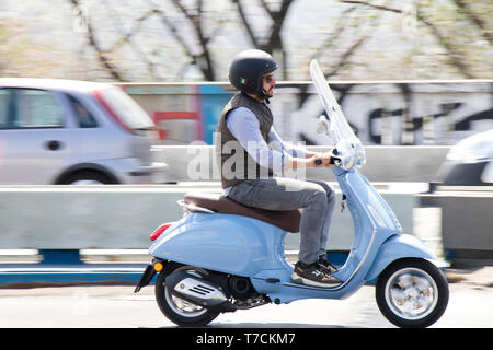 Belgrado, Serbia - Aprile 25, 2019: un uomo a cavallo azzurro scooter Vespa oltre il ponte in città il traffico della strada Foto Stock