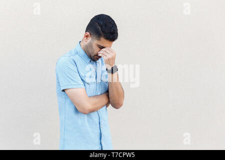 Problema, la depressione o la malattia. Ritratto di sola sad bel giovane uomo barbuto in maglietta blu in piedi tenendo la testa verso il basso e pianto. piscina studio Foto Stock