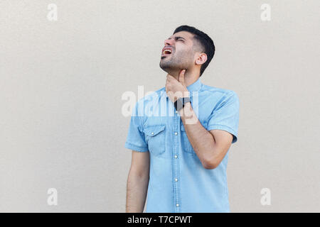 Gola il dolore, la malattia o il freddo influenza. Ritratto di malati bel giovane uomo barbuto in maglietta blu in piedi e tenendo il suo collo. piscina studio shot isolare Foto Stock