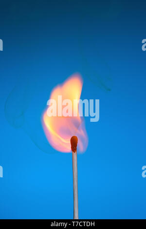 Fiammifero bruciato stickwith le fiamme e il fumo su sfondo blu Foto Stock