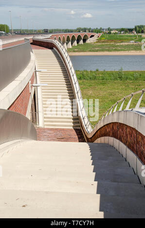 Nijmegen, Paesi Bassi, 25 Aprile 2019: calcestruzzo scale scendono dal ponte De Oversteek per le pianure alluvionali e il nuovo canale del fiume Foto Stock