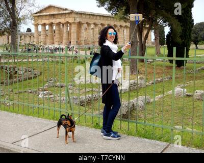 Donna turistico con il suo cucciolo di cane prende un selfie con il tempio di Nettuno in background in paestum italia Foto Stock