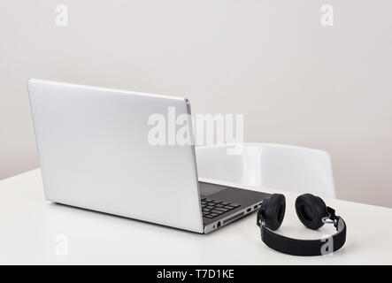 Nero cuffie wireless e un computer portatile su bianco tabella office Foto Stock