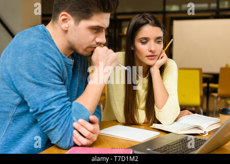 Foto di due giovani studenti amici matura in libreria studiare studiare leggere e utilizzando il computer portatile. Foto Stock