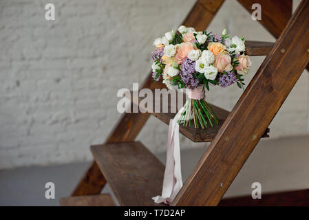 Bouquet di fiori di rose e lillà sorge su una scaletta di legno contro un bianco muro di mattoni Foto Stock