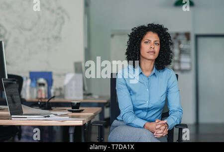 Fiducioso giovane imprenditrice seduto alla sua scrivania in un ufficio Foto Stock