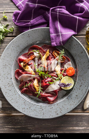 Carpaccio di manzo sulla piastra con pomodori secchi carciofi rucola e parmigiano Foto Stock