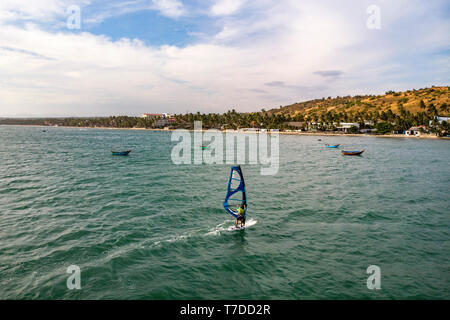 Mui Ne, Vietnam. Man Riproduci wind surf sport in mare sotto il vasto cielo blu Foto Stock