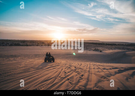 Due turisti ride su quad bike sulle dune di sabbia sullo sfondo di una splendida alba con un sole luminoso nelle prime ore del mattino. Safari in Vietnamese des Foto Stock