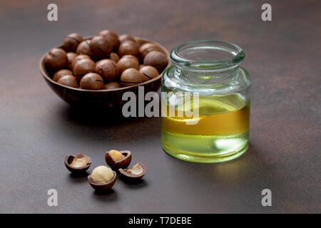 Olio di macadamia in una bottiglia di vetro, di noci di macadamia su uno sfondo marrone Foto Stock