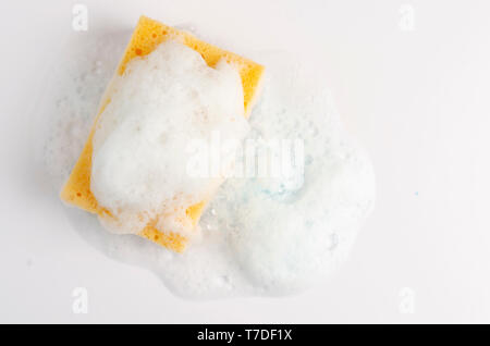 Giallo spugna insaponata con schiuma su sfondo bianco. Copia dello spazio. Foto Stock