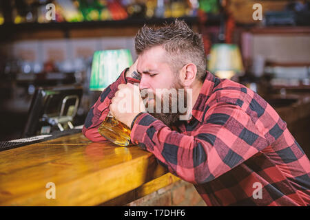 Uomo con barba trascorrere il tempo libero nella barra di colore scuro. Brutale parigamba uomo barbuto sedersi al banco bar bere birra. Hipster rilassante presso il bar con birra. Ordine di bere alcol. Il bar è un luogo rilassante hanno bere e rilassarsi. Foto Stock
