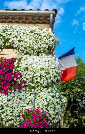 Francese bandiera nazionale sul vecchio edificio decorato con molti appesa coloratissimi fiori di petunia nella soleggiata giornata estiva Foto Stock