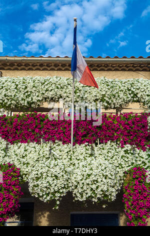 Francese bandiera nazionale sul vecchio edificio decorato con molti appesa coloratissimi fiori di petunia nella soleggiata giornata estiva Foto Stock