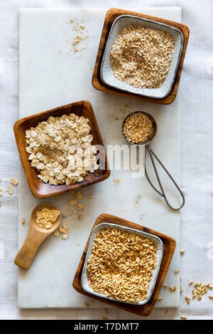 Chicchi d' avena, fiocchi d'avena e oat grist in ciotole di legno su marmo bianco bordo su sfondo bianco Foto Stock