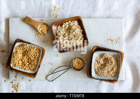 Chicchi d' avena, fiocchi d'avena e oat grist in ciotole di legno su marmo bianco bordo su sfondo bianco Foto Stock