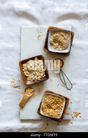 Chicchi d' avena, fiocchi d'avena e oat grist in ciotole di legno su marmo bianco bordo su sfondo bianco con spazio di copia Foto Stock