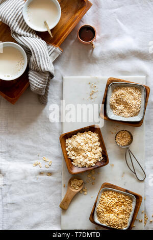 Chicchi d' avena, fiocchi d'avena, oat grist e Latte di avena in ciotole di legno e tazze bianche su marmo bianco bordo su sfondo bianco Foto Stock