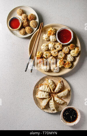 Dim sum Gyozas asiatici gnocco fritto parte insieme con una varietà di salse servito in piatti di ceramica e ciotole con bacchette su grigio Sfondo maculato. Foto Stock