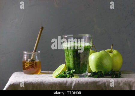 Gli spinaci verde kale apple frullato di miele in vetro su lino tovaglia con gli ingredienti di cui sopra. Salutare mangiare organico. Foto Stock