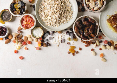 Varietà di frutta secca, noci, miele e fiocchi di avena in ciotole di ceramica per la cottura in casa sana colazione muesli muesli o barrette energetiche su bianco t Foto Stock