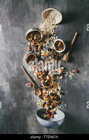 Varietà di frutta secca, noci, miele e fiocchi di avena si riversa nel vaso in ceramica per la cottura in casa sana colazione muesli muesli o barrette energetiche su bl Foto Stock