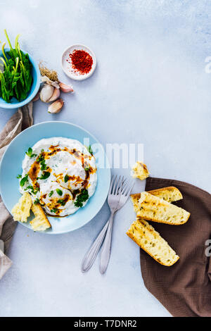 Bagno turco uova servite in una ciotola blu spruzzata con una salsa di burro accompagnata da spinaci, peperoncino rosso e pane tostato. Foto Stock