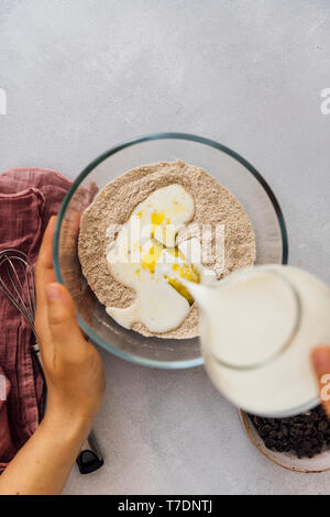 Donna versando il latte in secco di miscela di ingredienti in un recipiente di vetro. Foto Stock