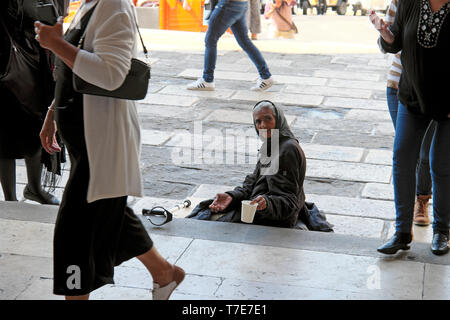 Povera anziana donna seduta sui gradini di una chiesa che tiene fuori una tazza e che chiede soldi mentre la gente cammina passato a Lisbona Portogallo Europa UE KATHY DEWITT Foto Stock