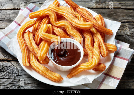 Close-up di churros - tradizionale Spagnola e Messicana dessert su una piastra bianca con salsa di cioccolato su un tavolo di legno con tovagliolo, vista orizzontale fro Foto Stock