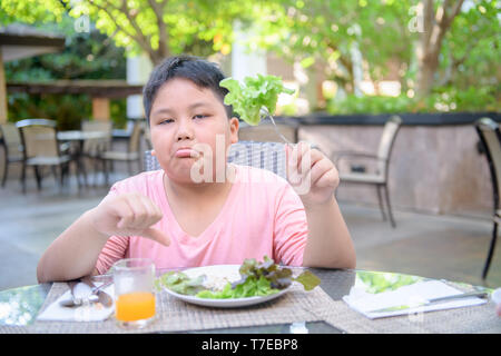 Obesi Fat Boy con espressione di disgusto contro le verdure in insalata, rifiutando il concetto di cibo Foto Stock