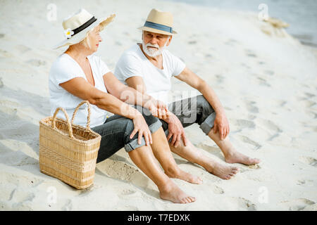 Bella coppia senior rilassante, seduti insieme sulla spiaggia sabbiosa, godendo della loro pensione vicino al mare Foto Stock